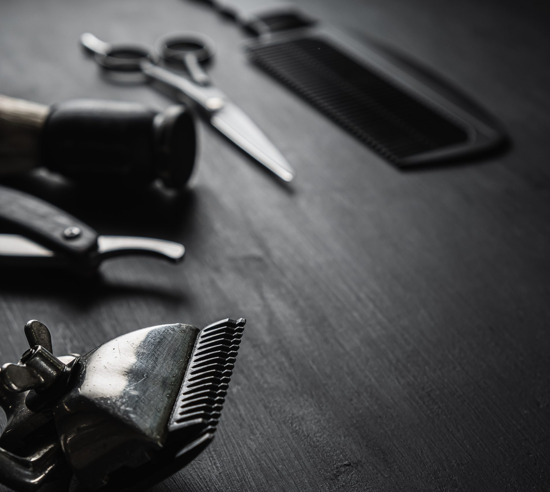 On a black dusty surface are old barber tools. Vintage manual hair clipper comb razor shaving brush shaving brush hairdressing scissors. black monochrome